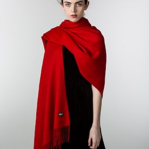 May include: A woman wearing a red shawl with fringe and a black dress. The shawl has a small black tag with the word "Silk" on it.