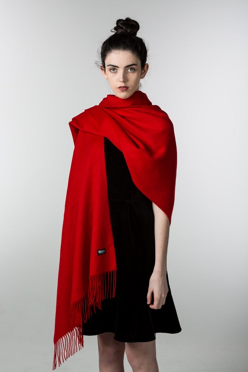 May include: A woman wearing a red shawl with fringe and a black dress. The shawl has a small black tag with the word "Silk" on it.