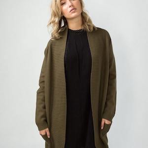 K&ouml;nnte beinhalten: Ein langer, olivgr&uuml;ner Cardigan mit Rippenstruktur und Taschen. Der Cardigan ist vorne offen und hat einen Schalkragen.