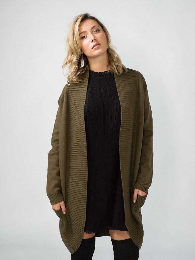 K&ouml;nnte beinhalten: Ein langer, olivgr&uuml;ner Cardigan mit Rippenstruktur und Taschen. Der Cardigan ist vorne offen und hat einen Schalkragen.