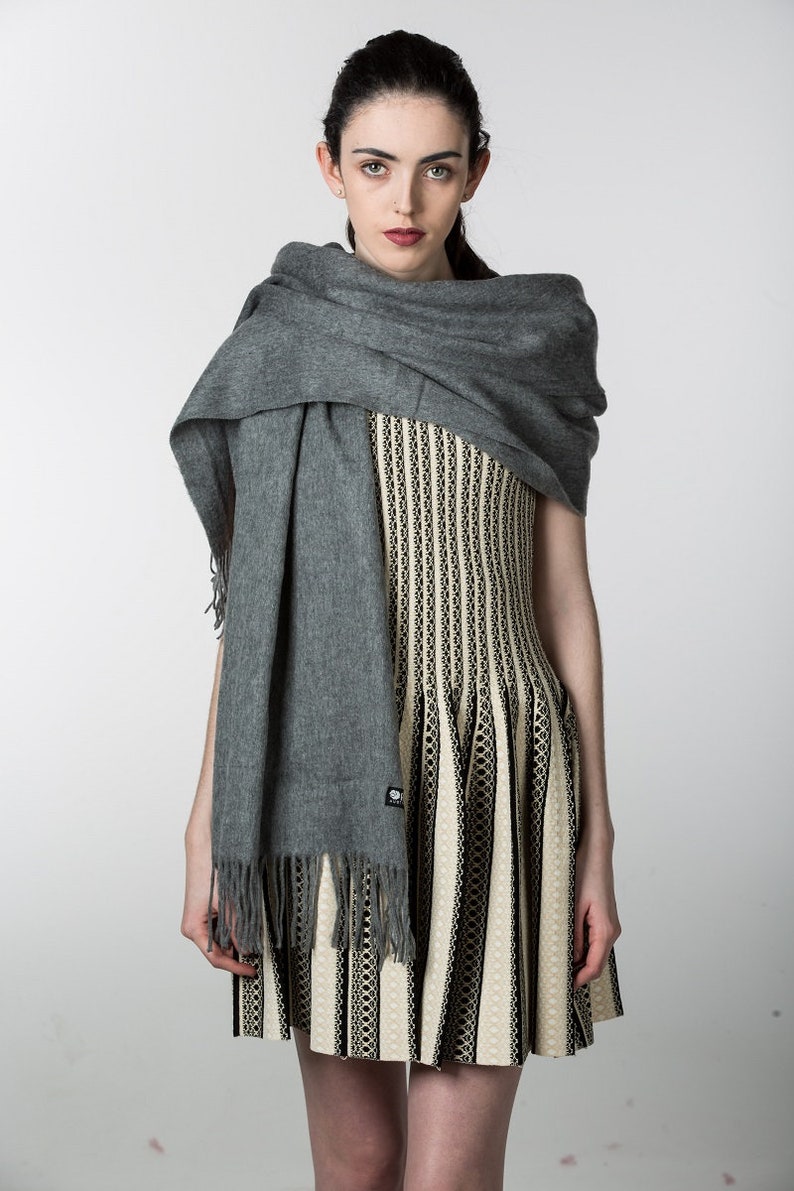 May include: A woman wearing a gray scarf over a black and white striped dress.