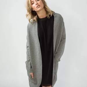 K&ouml;nnte beinhalten: Ein grauer gerippter Cardigan mit langen &Auml;rmeln und Taschen. Der Cardigan ist vorne offen und hat eine lockere Passform.