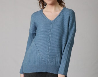 May include: A light blue v-neck sweater with a cable knit design. The sweater has long sleeves and a relaxed fit.