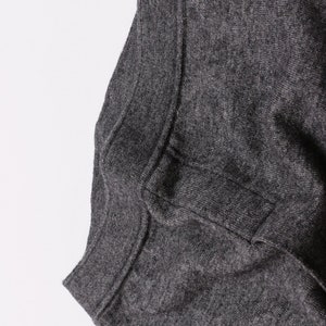 Puede incluir: Primer plano del tejido de punto gris de un su&eacute;ter. El tejido es suave y texturizado.