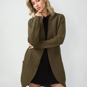 K&ouml;nnte beinhalten: Ein langer, olivgr&uuml;ner Cardigan mit Rippenstruktur und Taschen. Der Cardigan ist vorne offen und hat einen Schalkragen.