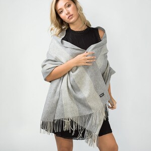 May include: A gray and white striped wool scarf with fringe. The scarf is draped around a person's shoulders.