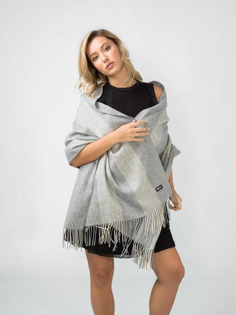 May include: A gray and white striped wool scarf with fringe. The scarf is draped around a person's shoulders.