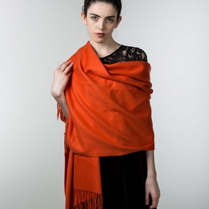 May include: A woman wearing a black dress with a lace top and a bright orange shawl with fringe.
