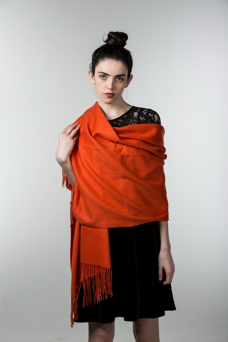 May include: A woman wearing a black dress with a lace top and a bright orange shawl with fringe.