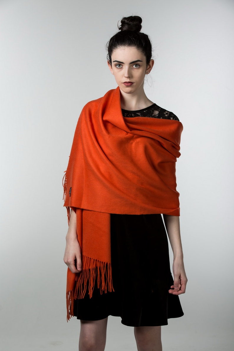 May include: A woman wearing a black dress with a bright orange shawl draped over her shoulders. The shawl has fringe along the bottom edge.