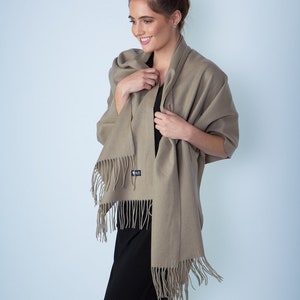 May include: A light brown shawl with fringe edges. The shawl is draped around a person's shoulders and is made of a soft, warm fabric.