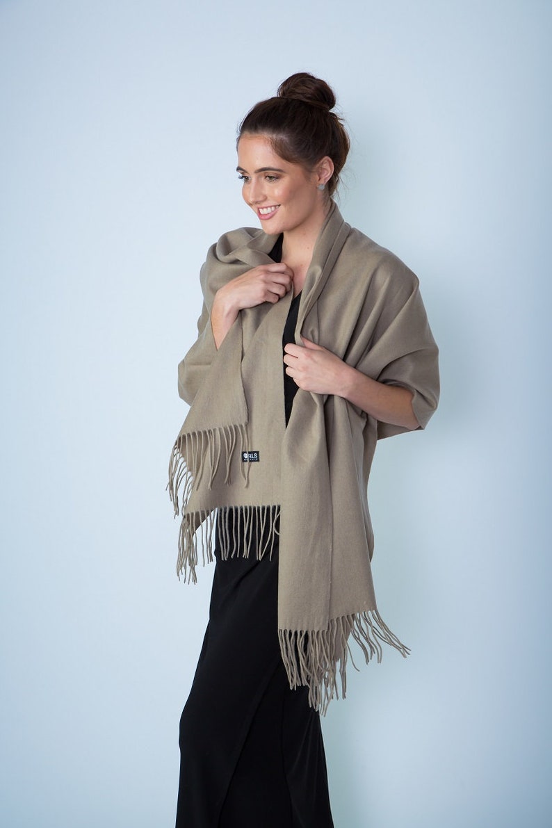 May include: A light brown shawl with fringe edges. The shawl is draped around a person's shoulders and is made of a soft, warm fabric.