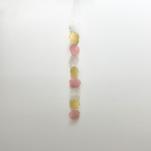 May include: A vertical strand of eight flat, flower-shaped beads arranged in a repeating sequence of translucent white, yellow, and pink. The beads are circular with five rounded petals each, strung together in a single column against a plain background.