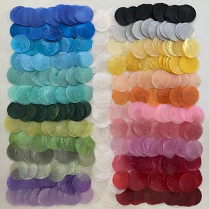 May include: A square arrangement of colorful, round, iridescent sequins. The sequins are arranged in vertical columns, showcasing a spectrum of colors from blues and greens to yellows, oranges, pinks, and reds. The sequins are evenly spaced, creating a visually appealing pattern.
