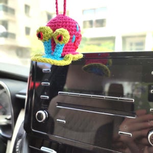 Pu&ograve; includere: Un ciondolo per auto a forma di lumaca all'uncinetto. La lumaca ha un corpo rosa con dettagli blu e rossi, occhi verdi con centri rossi e steli blu. Appeso a un cordino rosa, aggiunge un tocco giocoso agli interni.