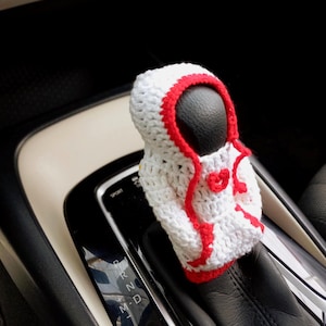 May include: White crocheted car gear shift cover with a red trim and a heart design.