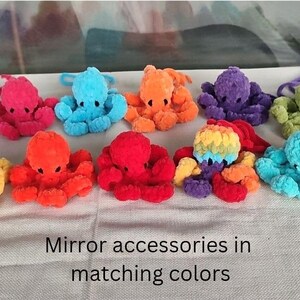 May include: A collection of colorful, plush octopus toys in various shades, including purple, pink, blue, orange, yellow, and green. The toys are arranged on a light-colored surface. The text "Mirror accessories in matching colors" is visible at the bottom.