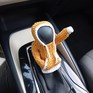 May include: A crocheted yellow and white hooded sweater gear shift cover for a car.