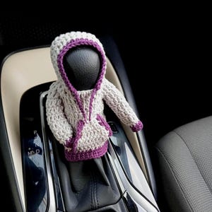 May include: A crocheted gray and purple hooded sweater gear shift cover for a car.