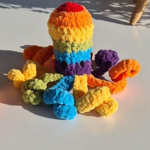 May include: A handmade, colorful crochet octopus toy. The octopus features a rainbow of colors, including red, orange, yellow, green, blue, and purple. The tentacles are also in various colors. This soft toy is suitable for children.
