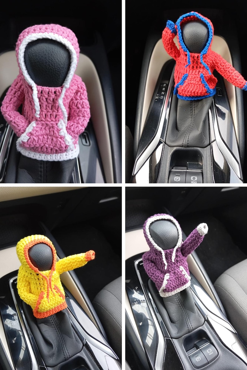 Puede incluir: Se muestran cuatro figuras con capucha de ganchillo en diferentes colores, rosa, rojo, amarillo y morado, en la palanca de cambios de un coche. Las figuras llevan sudaderas con capucha con ribetes blancos.