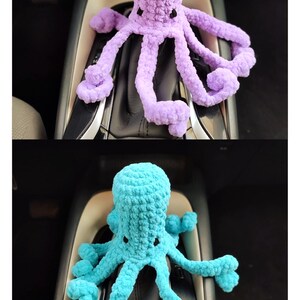 May include: Two crocheted octopus toys, one lavender and one turquoise, are displayed. The plush octopuses have multiple tentacles and small black eyes. The toys are sitting on a car's gear shift console.