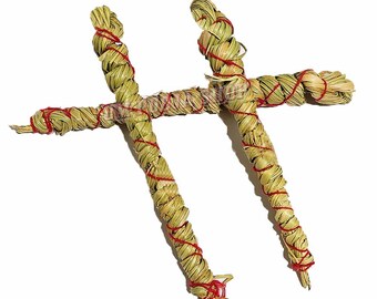 May include: Two bundles of dried grass, each tied with red string, are twisted into a cross shape.