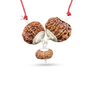 Pode incluir: Um colar de três contas com um cordão vermelho e detalhes prateados. As contas são marrons e têm uma textura áspera. O colar é de estilo tradicional indiano.