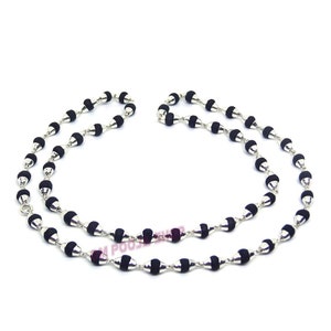 Puede incluir: Un collar de cuentas negras y plateadas con un cierre plateado. Las cuentas son redondas y tienen una forma ligeramente puntiaguda.