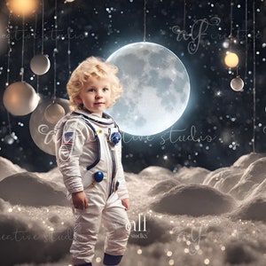 Puede incluir: Un niño pequeño vestido con un traje de astronauta blanco se encuentra en un paisaje nevado similar a la luna. El niño está mirando hacia la derecha del marco. Una gran luna brillante cuelga en el cielo sobre el niño. El fondo es azul oscuro con estrellas blancas y una cadena de adornos blancos y dorados que cuelgan de la parte superior del marco.