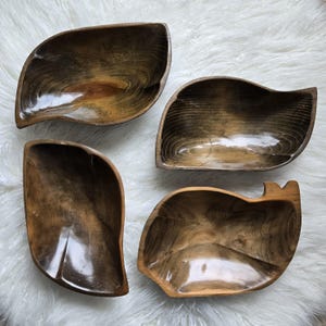 May include: Four wooden bowls in various shapes and sizes. The bowls are all dark brown with a glossy finish. They are arranged on a white fuzzy surface.