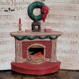 May include: A vintage Christmas decoration featuring a fireplace with a brick hearth and a mantel decorated with a green wreath, a clock, a candle, and a book. The background is a white sheet of music with the words "Nuts Roasting" and "Tree Here" printed on it.