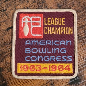 May include: A maroon fabric patch with white stitching around the edges. The patch features a red square with a white bowling pin and the letters "ABC" in white. The text "League Champion" is in yellow, "American Bowling Congress" is in blue, and "1963-1964" is in red and yellow.