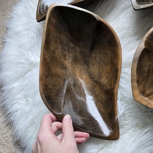 May include: A set of three wooden bowls, each with a unique shape and a dark brown wood grain. The bowls are made of natural wood and have a rustic, handcrafted look.