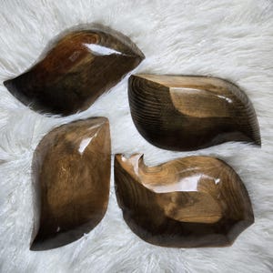 May include: Four wooden bowls with a dark brown finish. The bowls are shaped like leaves and have a smooth, polished surface.