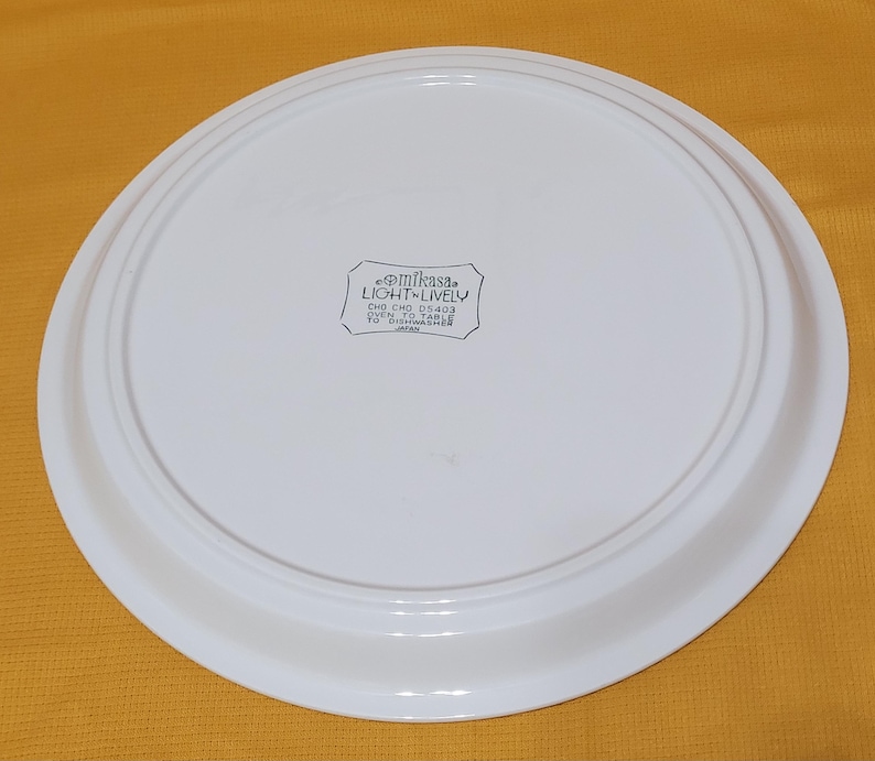Pu&ograve; includere: Piatto da portata in ceramica bianca con un bordo rialzato. Il fondo del piatto ha un adesivo bianco e nero che recita "Mikasa Light 'n Lively  DNO CHO 05403 Oven to Table  Safe for Dishwasher  Japan."