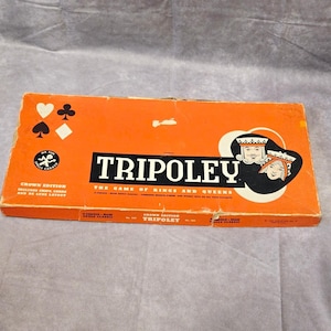 May include: An orange box for the game Tripoley, featuring the text "Tripoley" in large, bold letters. The box includes illustrations of playing card suits and a king and queen. The game is described as "The Game of Kings and Queens."