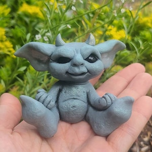 May include: A small, gray, sculpted figurine of a creature with large ears, a pointed tail, and a mischievous expression. The figurine is sitting with its legs crossed and its hands clasped in front of it.