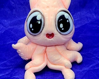 May include: A pink and white squid figurine with large, cartoon eyes. The squid has a small, red mouth and is sitting on a blue surface.