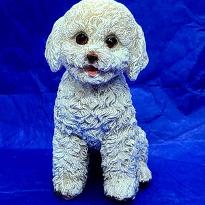 May include: White ceramic figurine of a sitting poodle with brown eyes and a pink nose. The poodle has a fluffy white coat.