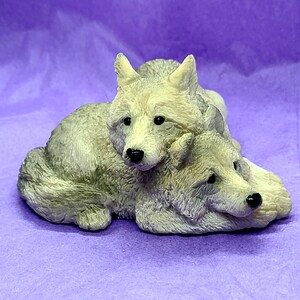 May include: Two grey wolf figurines cuddling together. The wolves are made of a smooth, white material and have realistic features.
