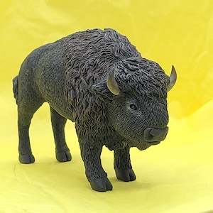 May include: A black bison figurine with a shaggy coat and short horns. The figurine is standing on a yellow surface.