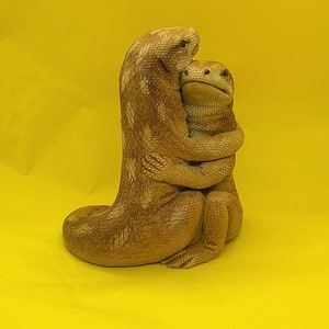May include: A brown ceramic sculpture of two lizards hugging each other. The lizards are sitting on a yellow surface.