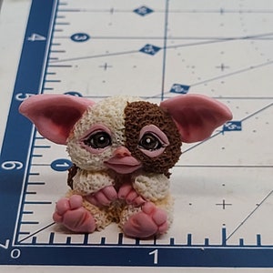 May include: A small, brown and white furry toy with pink ears and feet. The toy is sitting on a blue and white surface.
