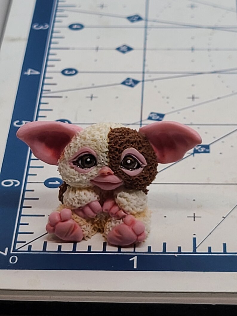 May include: A small, brown and white furry toy with pink ears and feet. The toy is sitting on a blue and white surface.