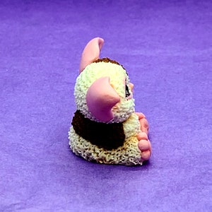 May include: A small, white and brown fuzzy toy with pink ears and feet. The toy is sitting on a purple surface.