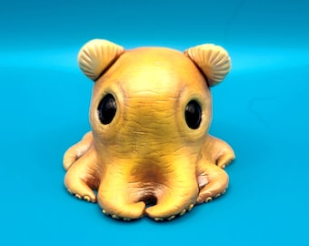 May include: A whimsical, yellow octopus figurine with large, black eyes and small ear-like appendages. The octopus has eight tentacles and is set against a bright blue background. The figurine has a textured surface and a cartoonish design.