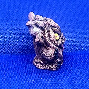 K&ouml;nnte beinhalten: Eine kleine, braune und graue, detaillierte Keramikfigur eines Wesens mit einem einzigen gelben Auge. Das Wesen hat eine strukturierte Oberfl&auml;che und scheint ein Monster oder eine mythische Kreatur zu sein.