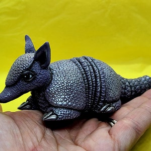 May include: A small, purple and silver armadillo figurine with a detailed shell and a textured surface.