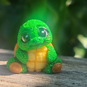 May include: A small green turtle figurine with large eyes and a yellow shell. The turtle is sitting on a wooden surface.
